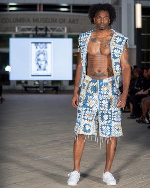 Model showcases blue and white patterned shorts with fringe detail on fashion runway.