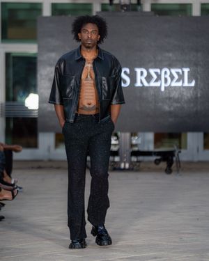 Fashion model walks runway wearing black leather jacket and orange top at Columbia Museum of Art fashion show.