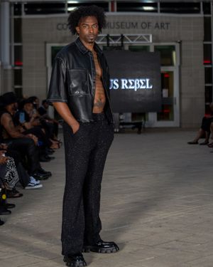 Model showcases black avant-garde streetwear ensemble on runway at Columbia Museum of Art.