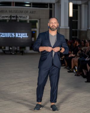 Model walks runway wearing navy blue suit during fashion show at Tampa Museum of Art.