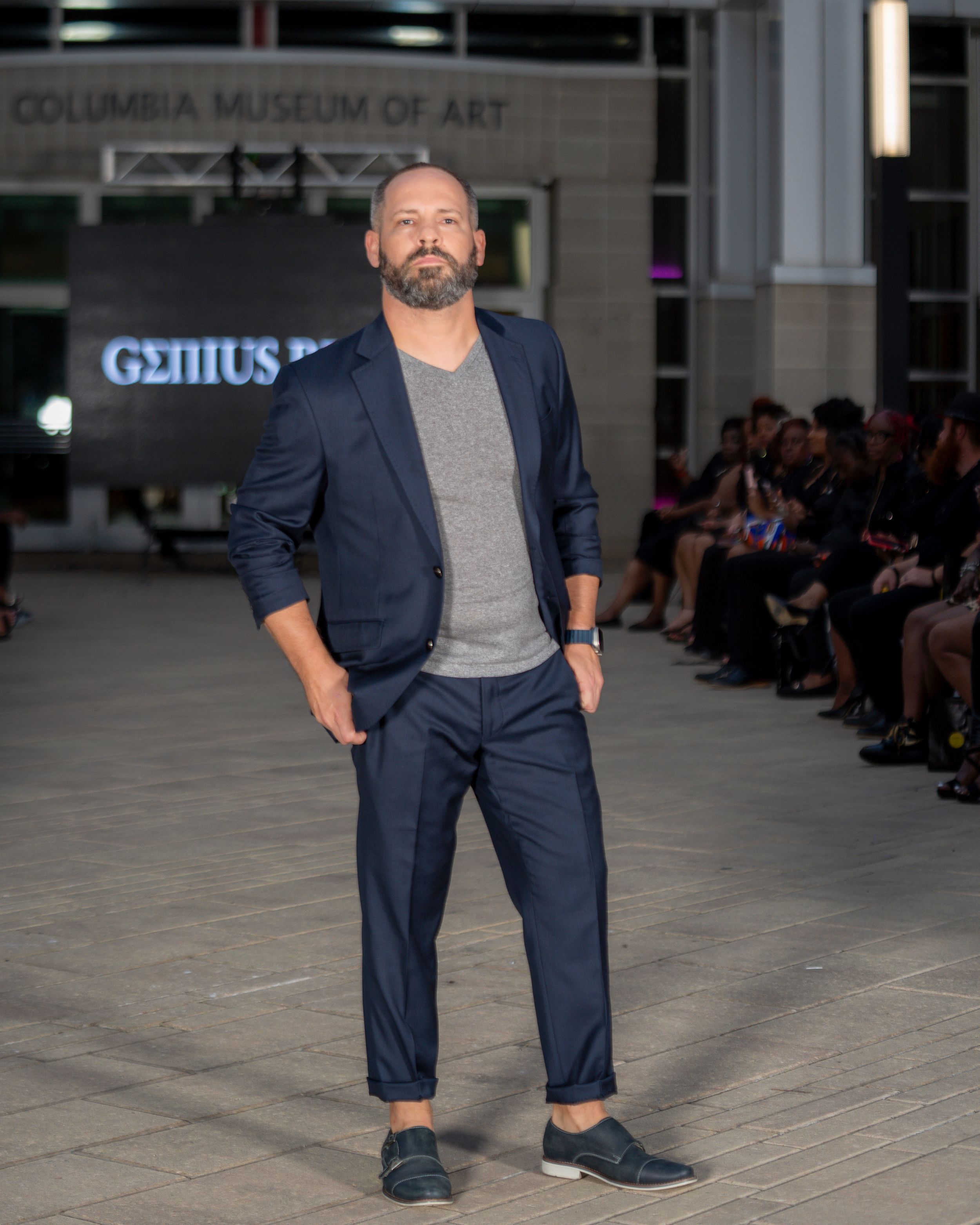 Model showcases navy suit with grey t-shirt combination on industrial-style runway.