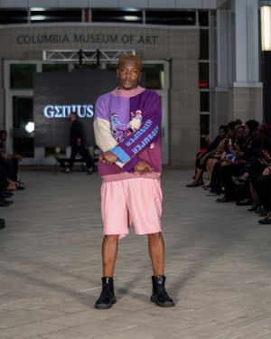 Model showcases pink shorts and purple top ensemble during museum fashion show.