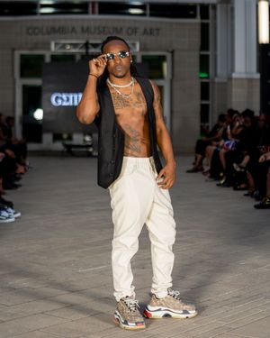 Model showcases white cargo pants and sneakers on industrial runway setting.