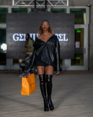 Model struts down runway in black leather boots and orange accessories.