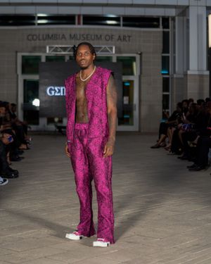 Fashion model walks runway in vibrant magenta snakeskin print jumpsuit at Columbia Museum of Art fashion show.