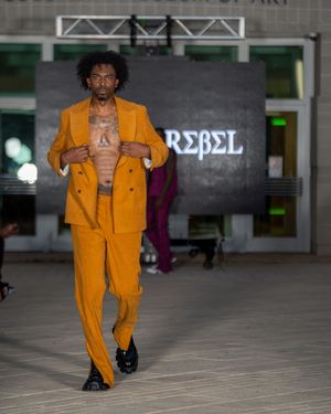 Model walks runway in bright orange utility jacket and matching pants ensemble.