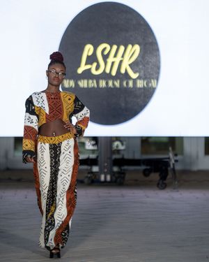 Model showcases colorful patchwork dress with geometric patterns on fashion runway.