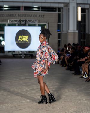 Model showcases floral print dress with combat boots at fashion show.