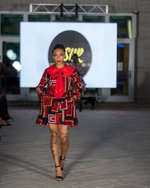 Runway model wearing bold red geometric pattern outfit during fashion show performance.