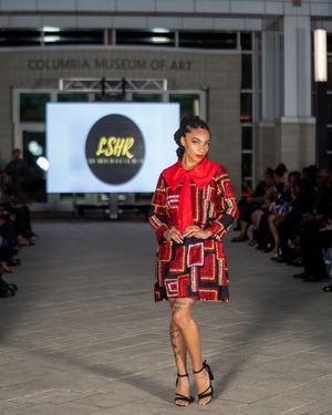 Fashion model walks runway in red and black geometric patterned ensemble at Columbia Museum of Art fashion show.