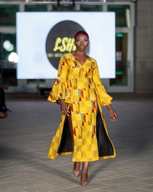 Model walks runway in bright yellow avant-garde coat with geometric cutouts during fashion show.