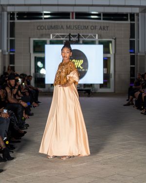 Elegant champagne-colored ball gown with metallic accents displayed at museum fashion show.