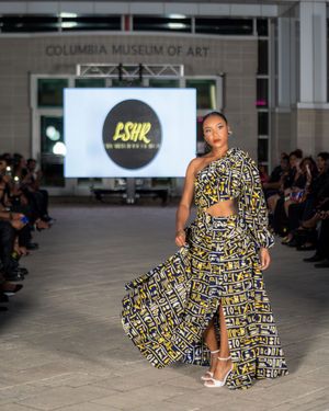 Model presents flowing geometric print dress in black and yellow pattern on museum runway.
