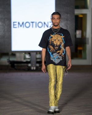 Model struts down catwalk wearing black t-shirt with graphic print and yellow metallic pants.