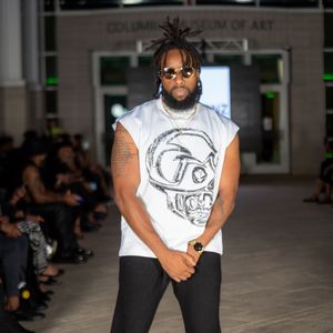 White graphic t-shirt with black pants modeled on indoor catwalk.