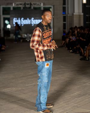 Model walks runway in casual plaid shirt and distressed denim jeans at fashion show.