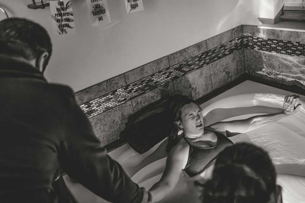Black and white photograph showing a person lying on a bed with patterned wallpaper in the background.