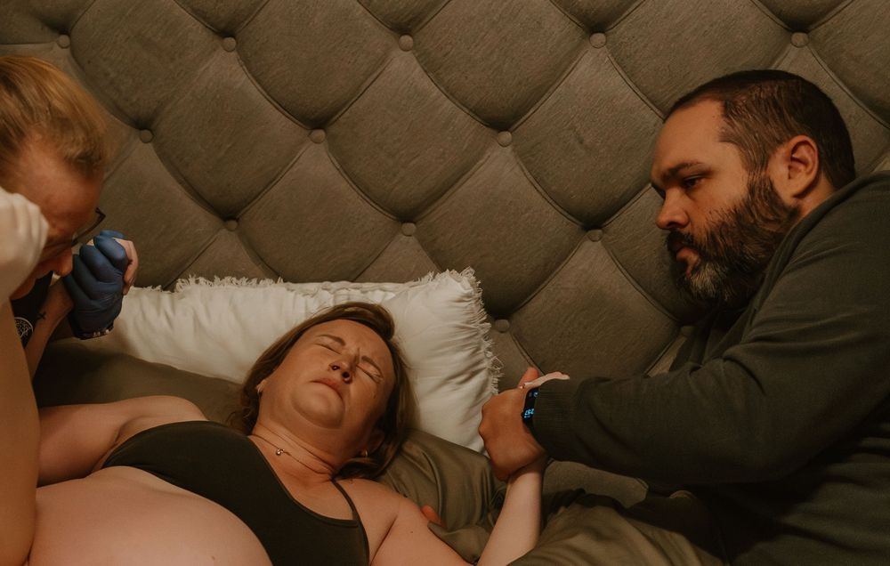 A group of people lie together on a tufted leather couch in a dimly lit room.