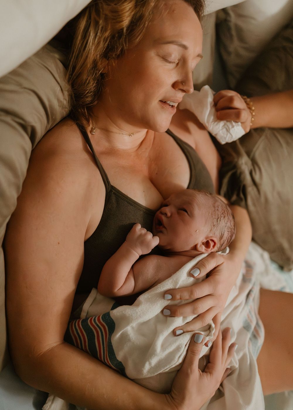 Intimate series of photos showing a parent bonding with their newborn baby in bed.