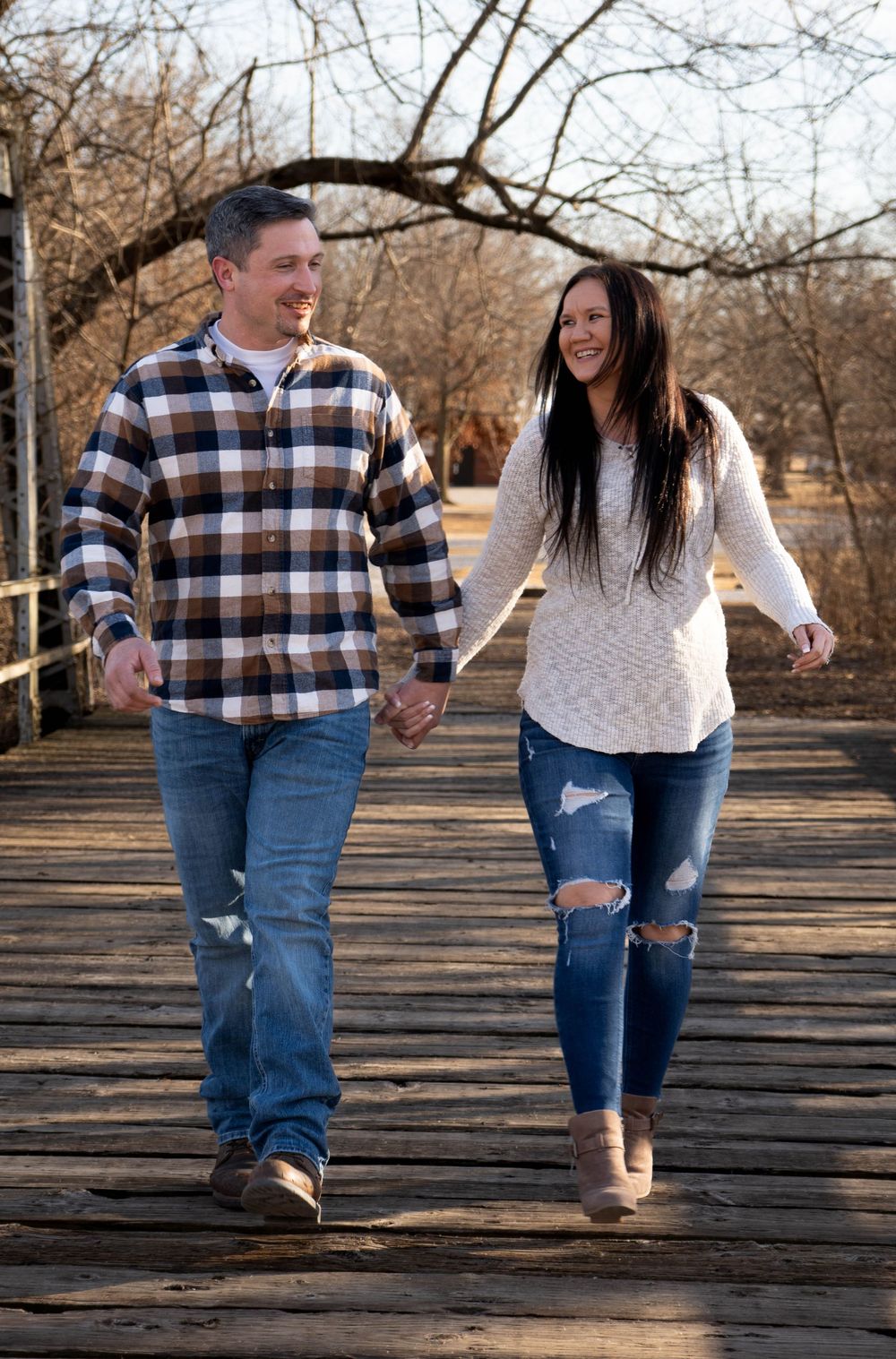 Smiling couple walking hand in hand on a rustic wooden bridge in winter.