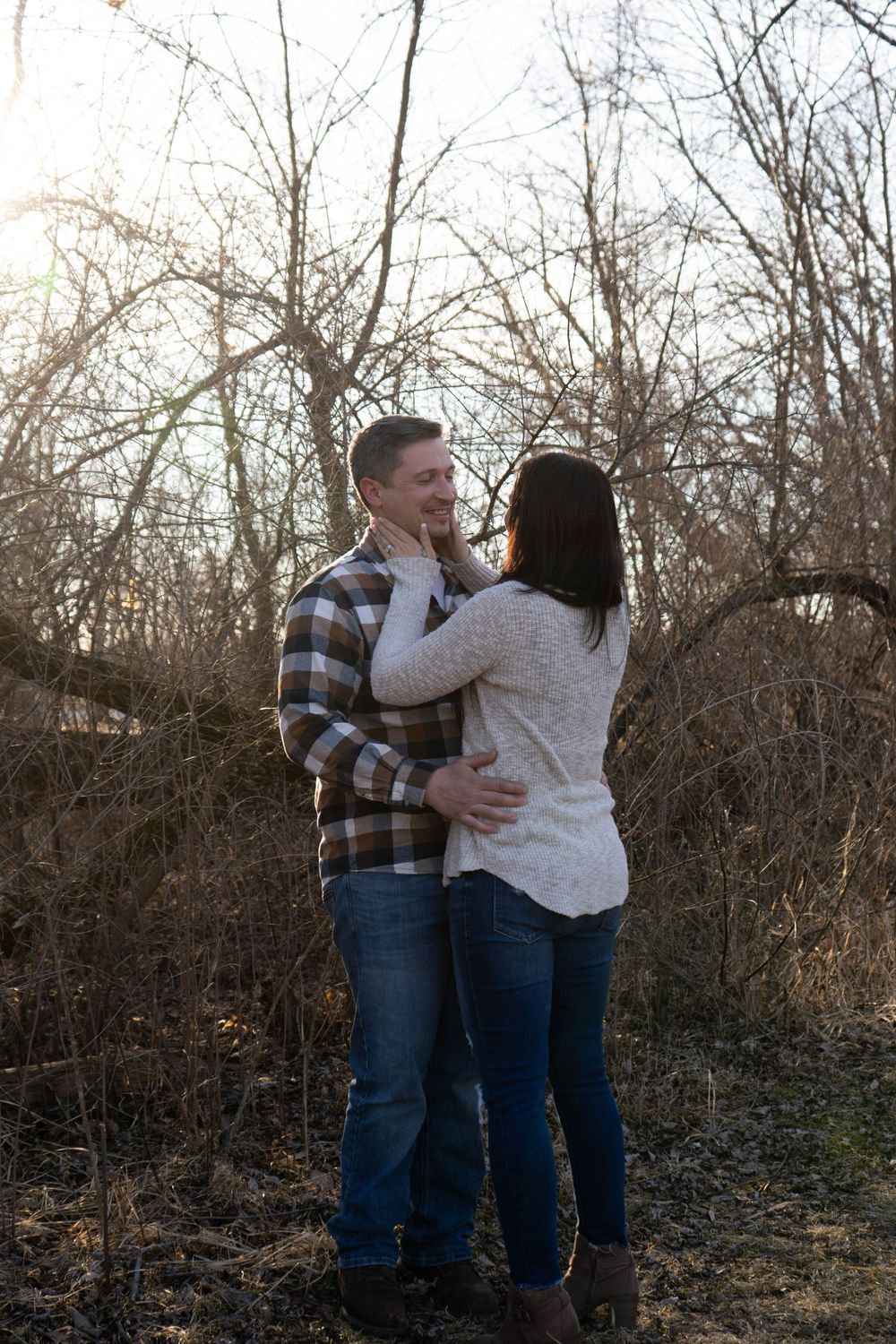 Couple embracing romantically among bare winter trees in an outdoor engagement photo session.