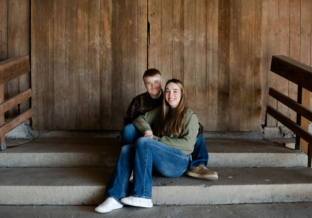 Young couple sitting together on steps in front of rustic wooden barn doors.