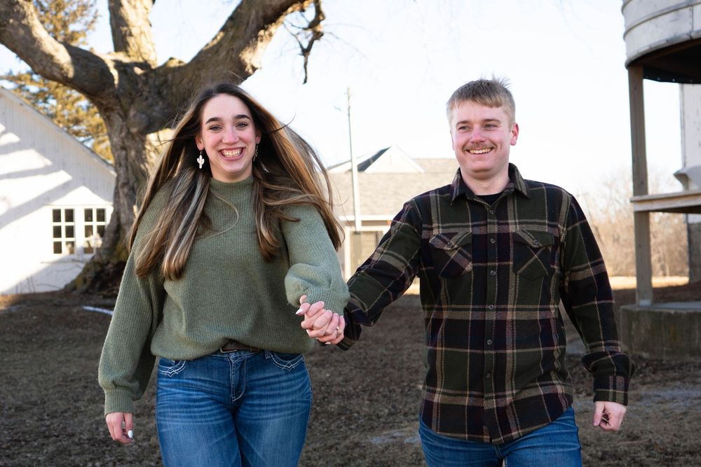 Happy couple holding hands and walking outdoors near a large tree in winter.
