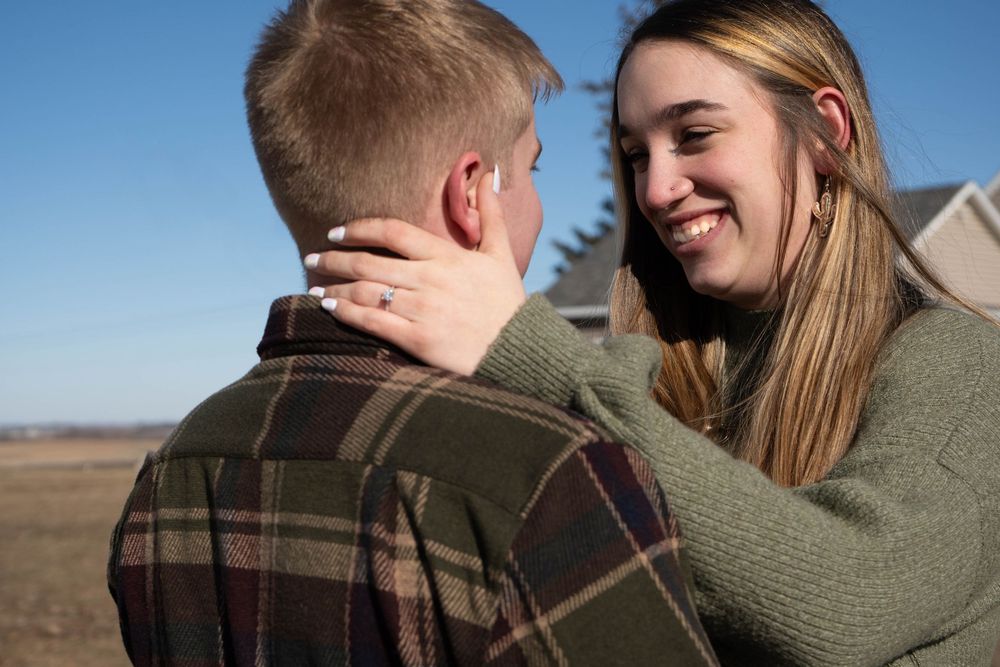 Smiling woman embracing man outdoors under clear blue sky in casual attire.
