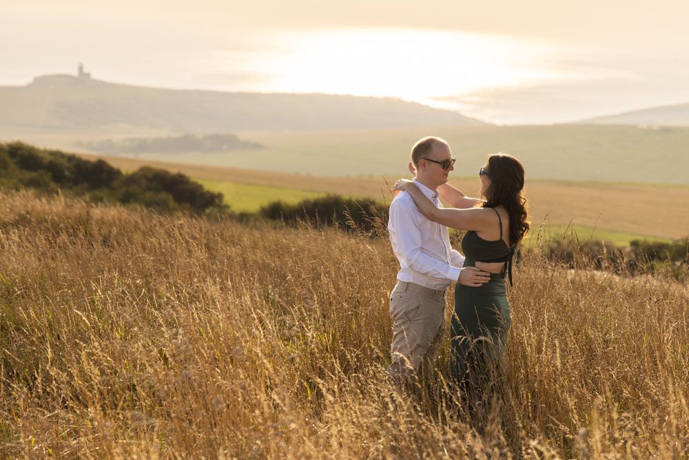 Couple in embrace with large landscape scene of East Sussex countryside and seascape