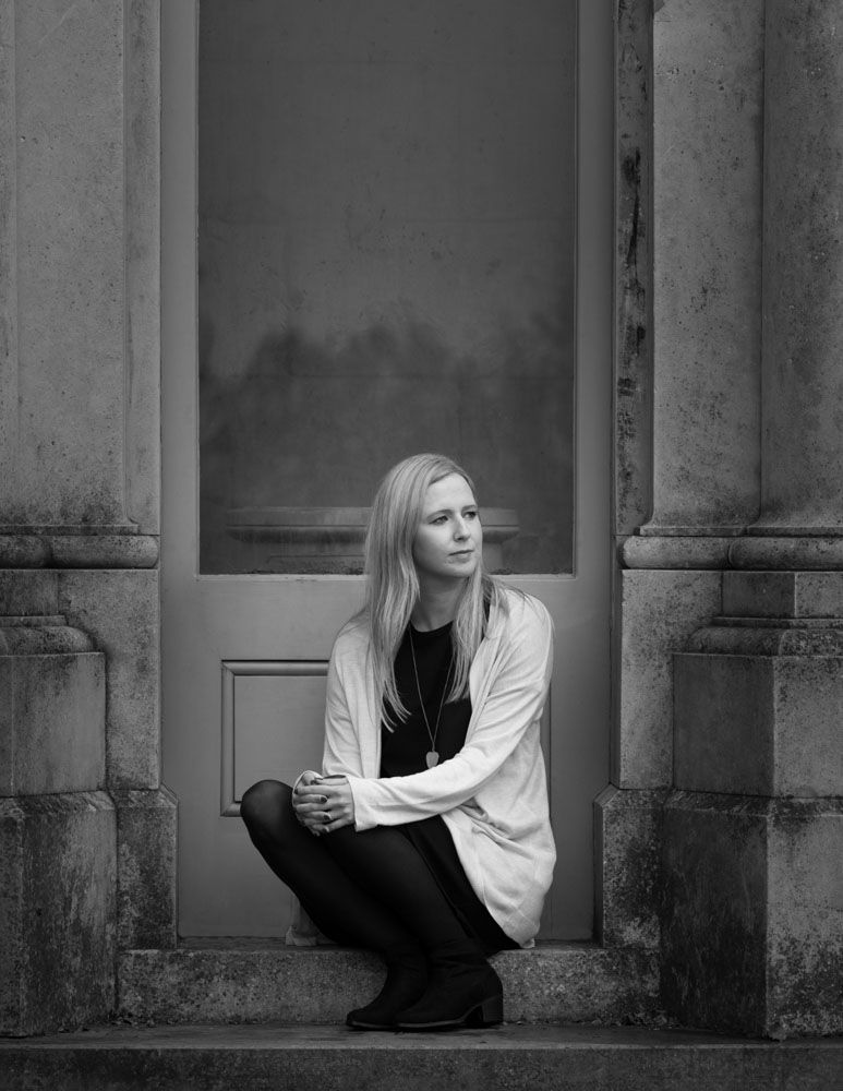 Young woman kneels elegantly on steps of historic folly