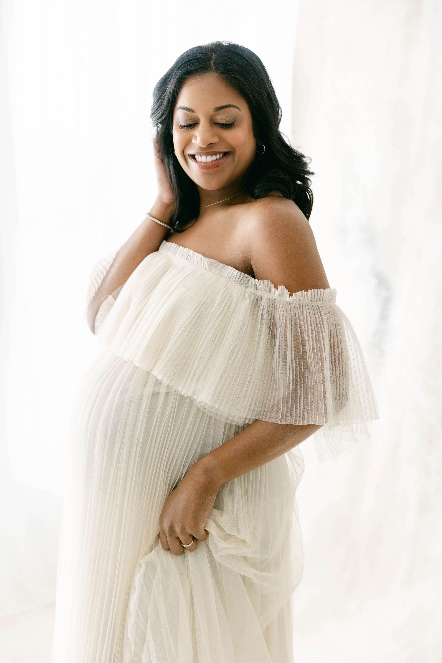 Three elegant maternity photos show a woman in a flowing white off-shoulder pleated dress against a bright background. Connecticut Studio.