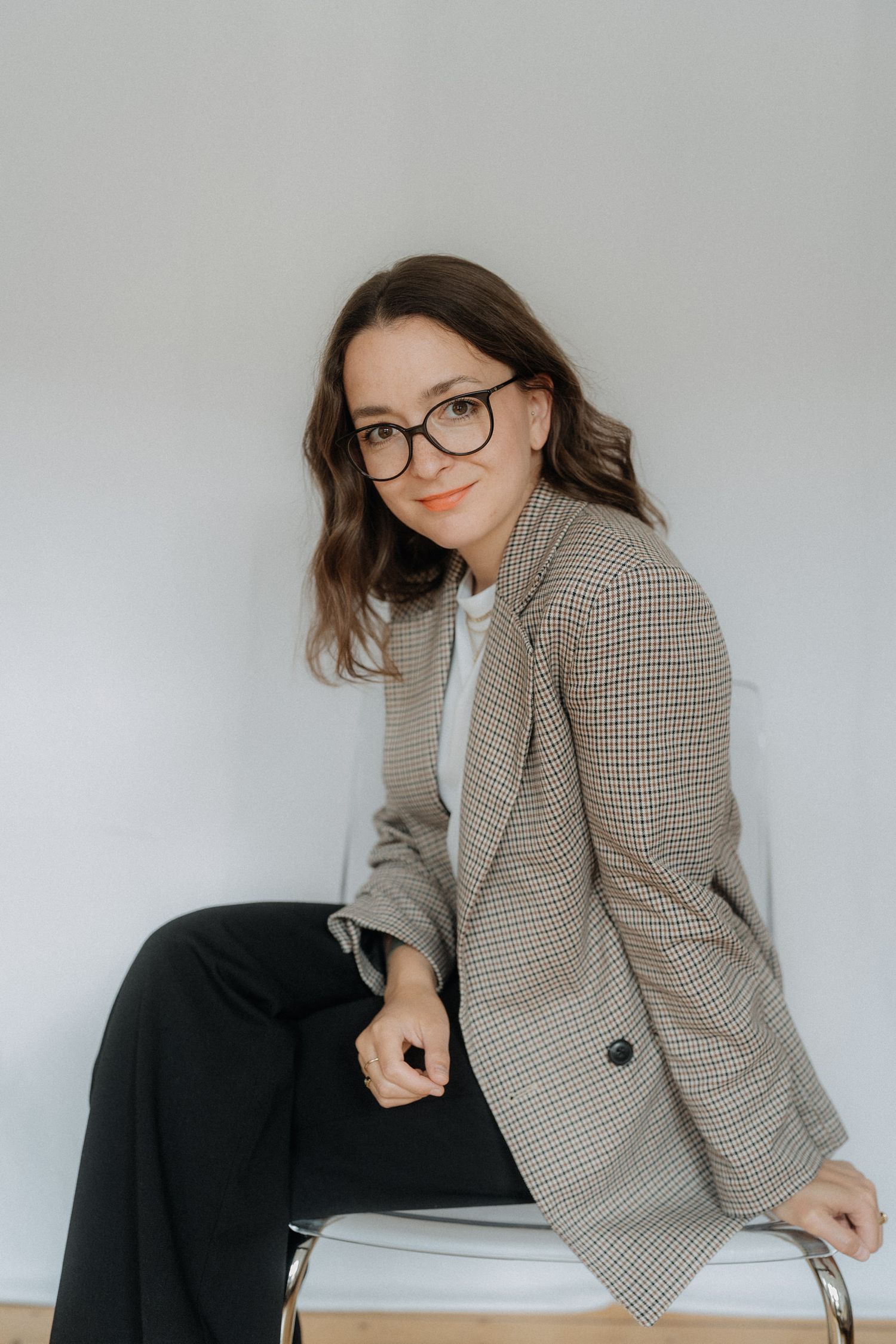 A series of fashion photos showing someone wearing a chic plaid blazer and glasses in various seated poses.