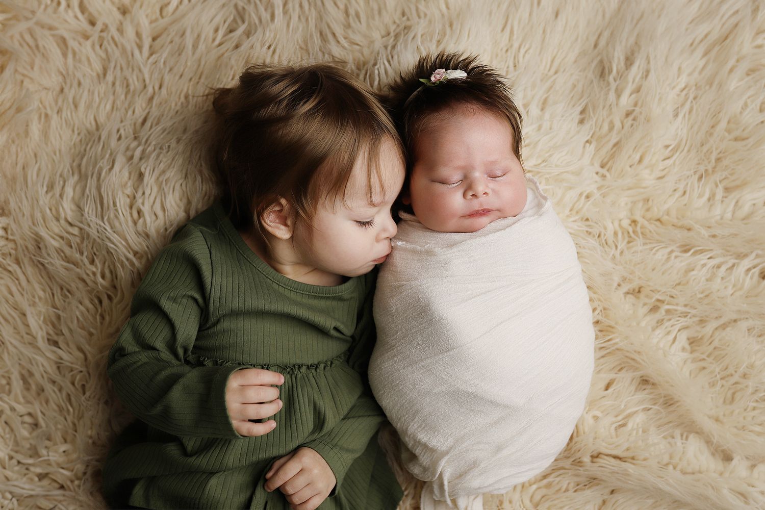 Two siblings share a tender moment on a cozy cream-colored blanket. Utah County newborn photographer. Orem baby photos