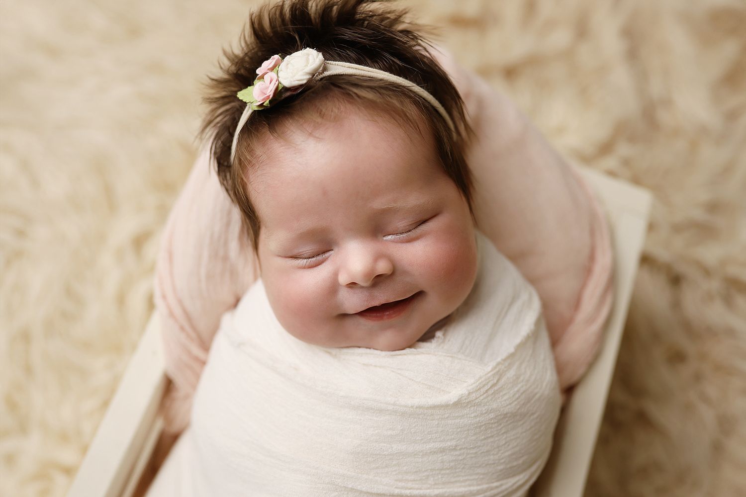 Newborn baby wrapped in soft white fabric sleeping peacefully on a cream-colored textured backdrop. Utah County baby photographer