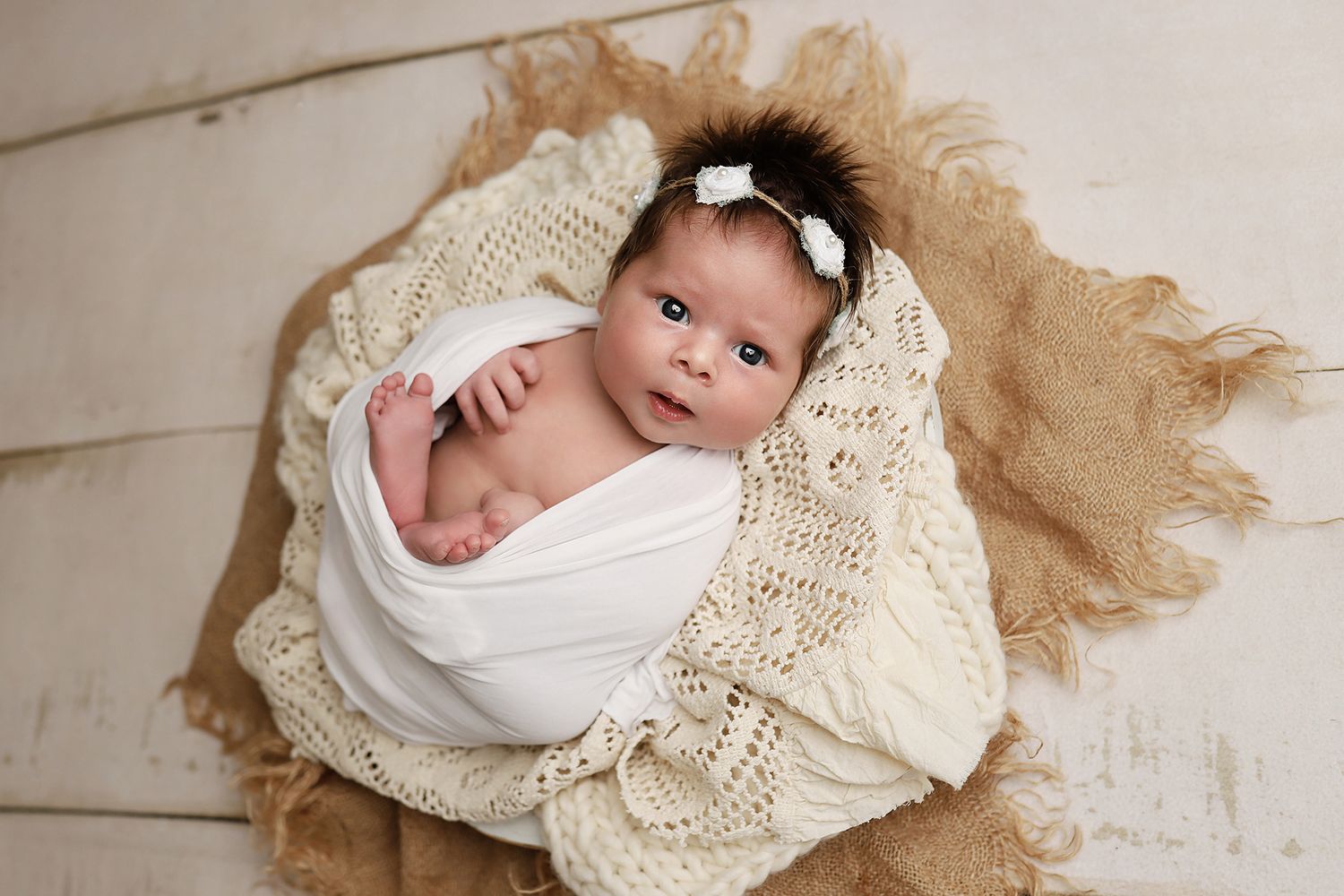 Sleeping newborn baby wrapped in white swaddle blanket on cream lace backdrop with rustic wood floor. Utah newborn photography