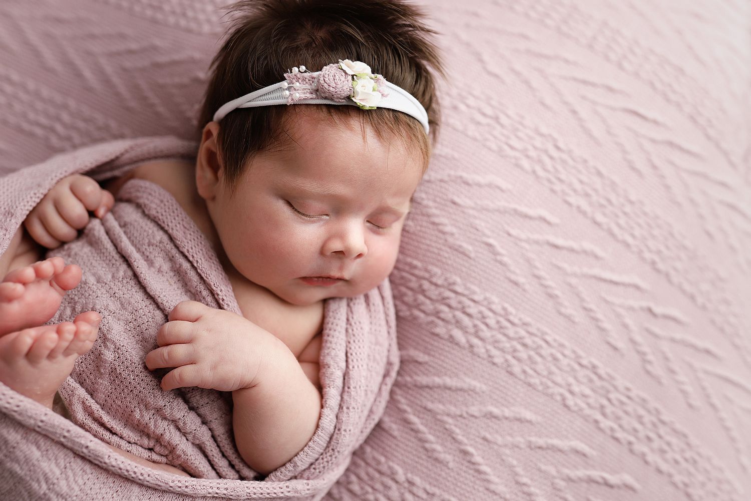 A sleeping newborn baby swaddled in soft pink fabric is captured in a series of peaceful poses during a photoshoot. Utah newborn photos