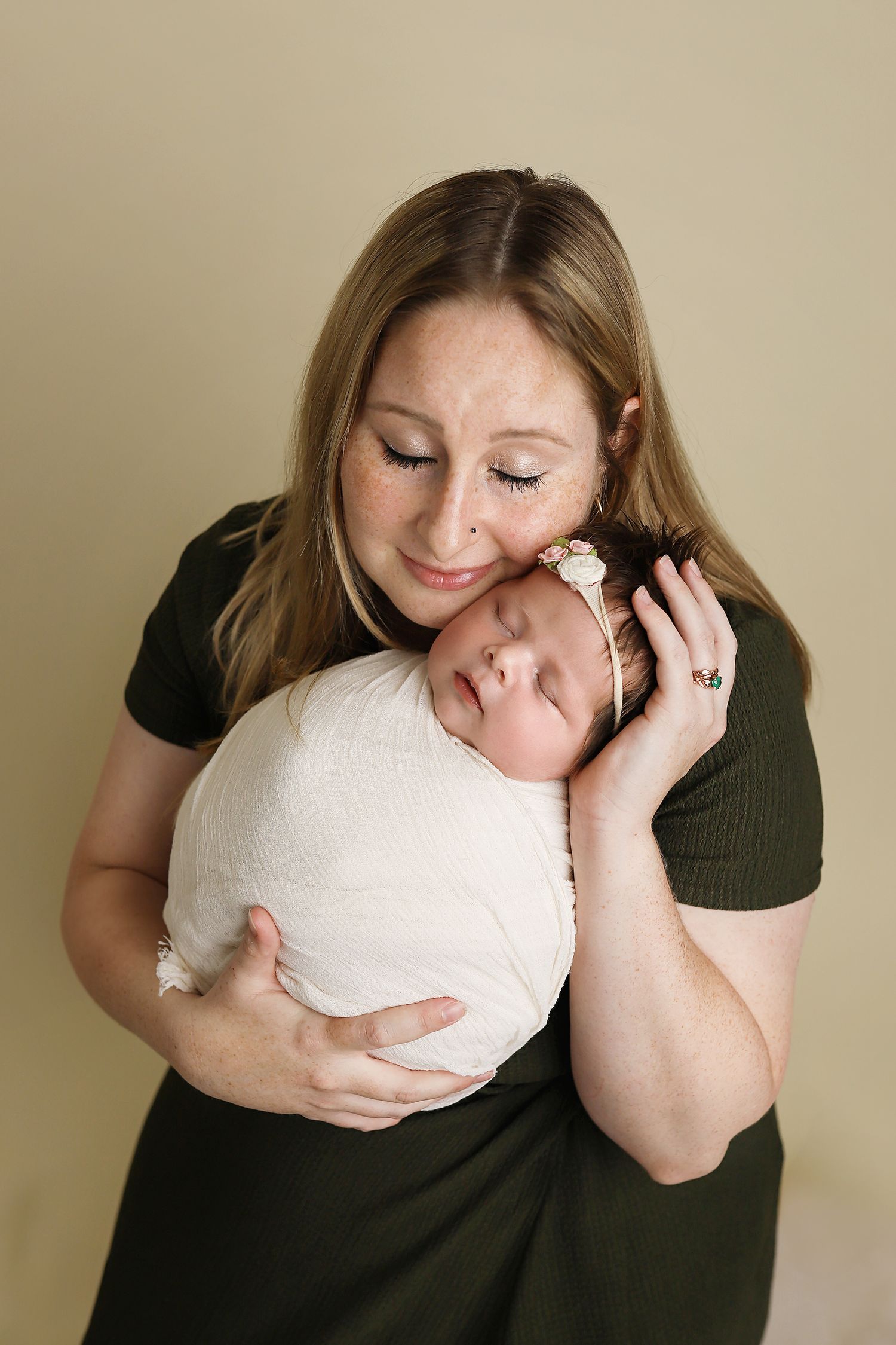 A sequence of photos showing someone in a dark green top hugging a white heart-shaped pillow against a beige wall. Utah newborn photos.