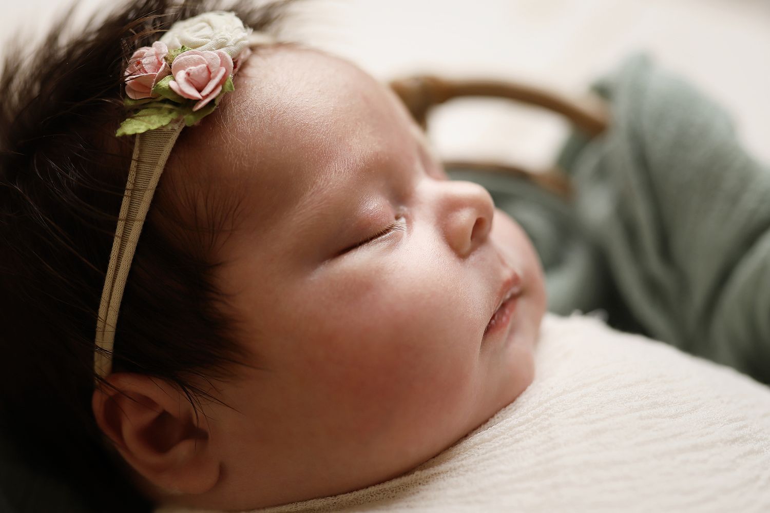 Close up view of a sleeping newborn baby with dark hair resting peacefully against a light colored background. Utah baby photos