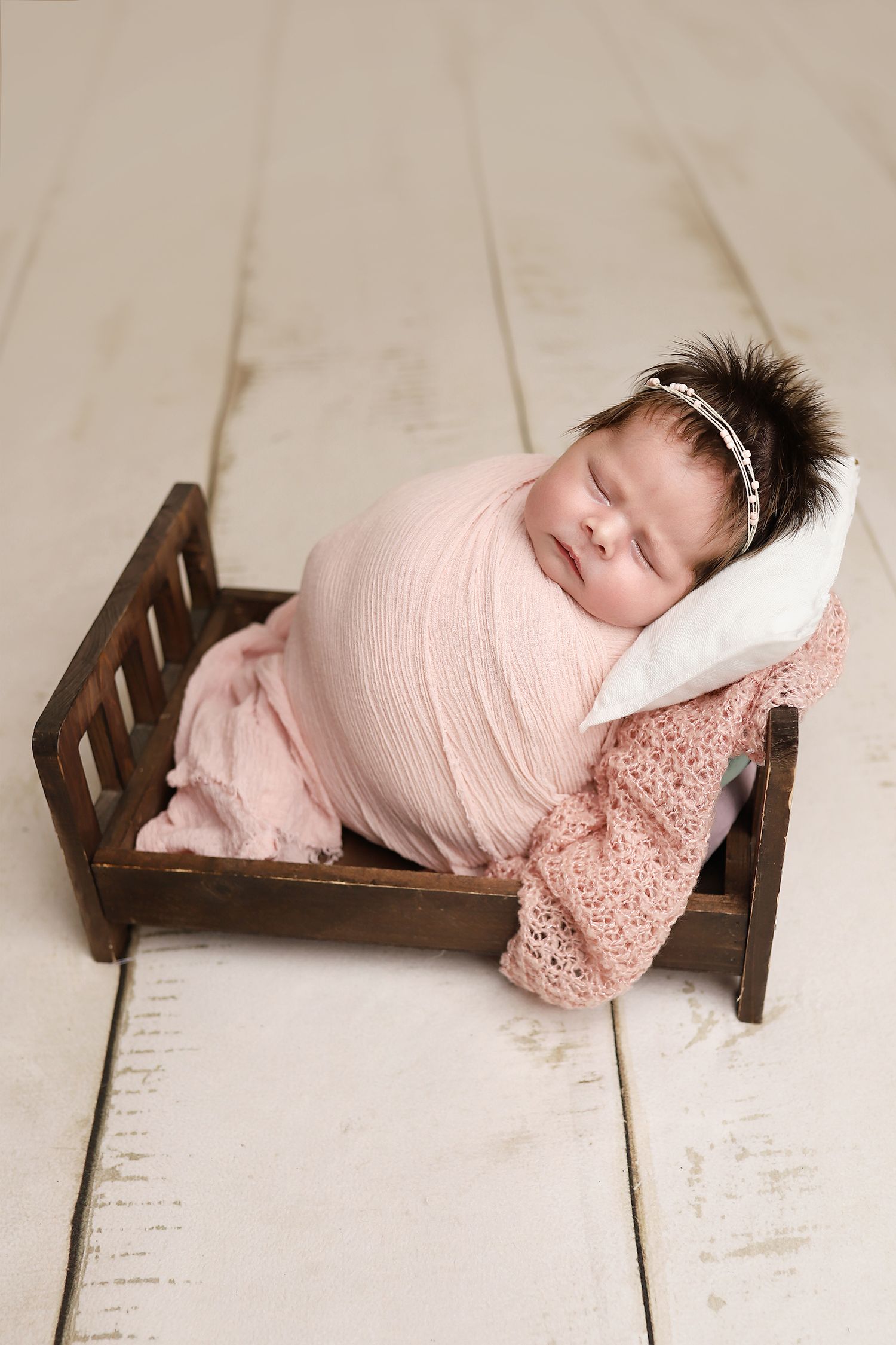 A newborn baby wrapped in pink swaddle lying on a small wooden bed in a series of four connected photos. Utah county newborn photographer
