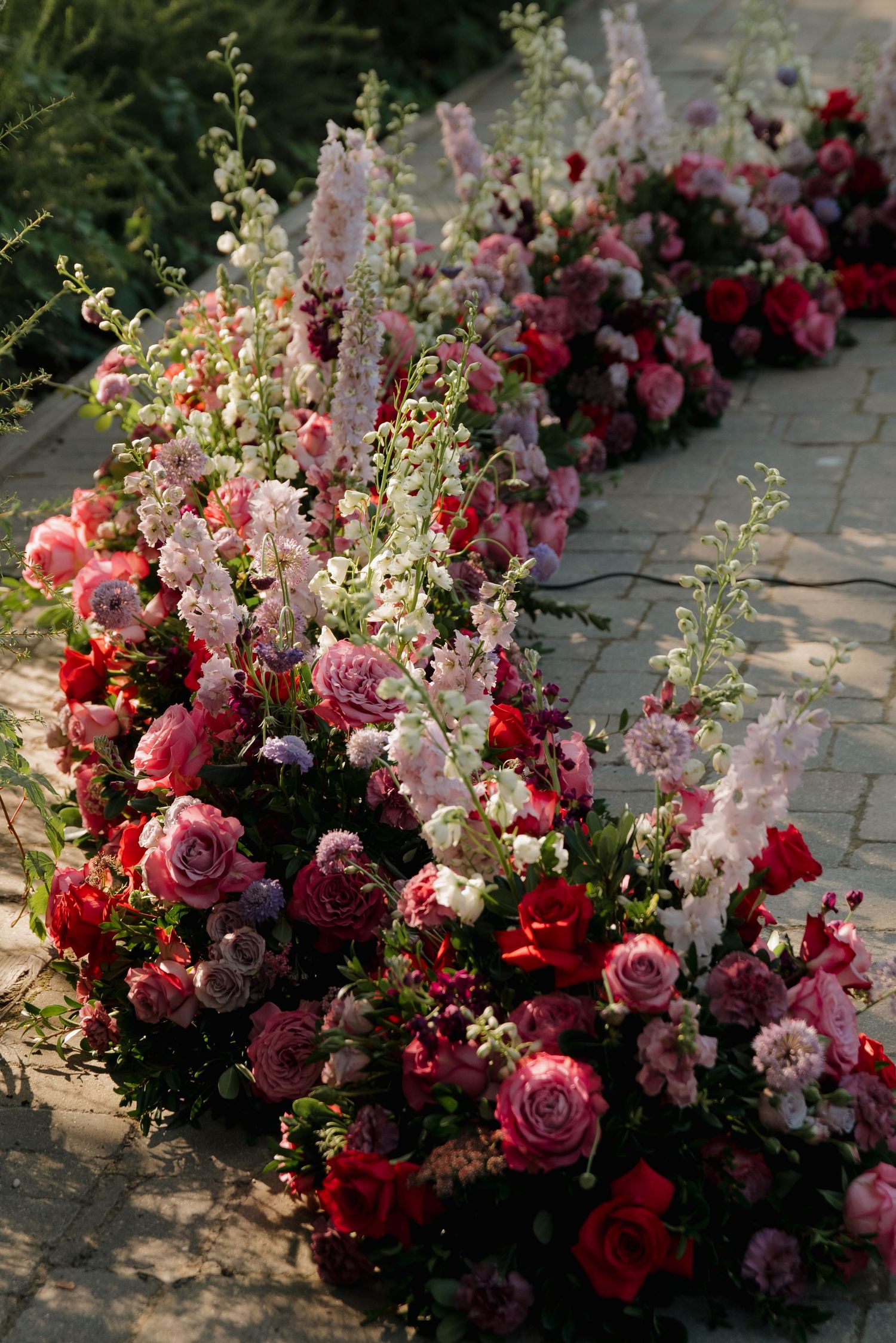 Lush floral arrangement featuring pink and red roses with delicate white flowers cascading along a stone pathway.