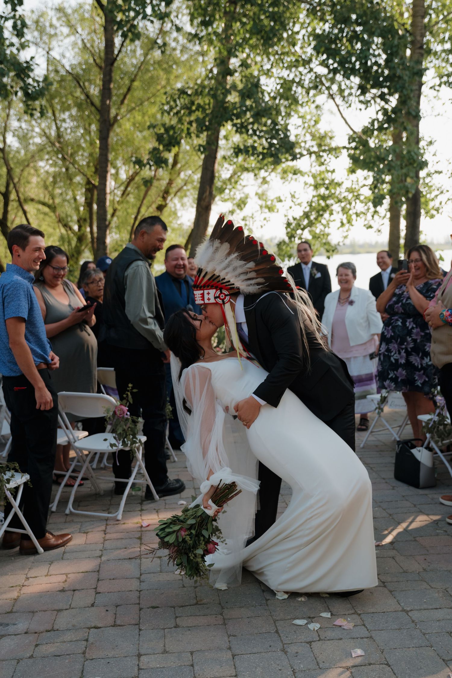 A wedding couple performs a fun dip dance move on a brick patio surrounded by guests during their reception celebration.