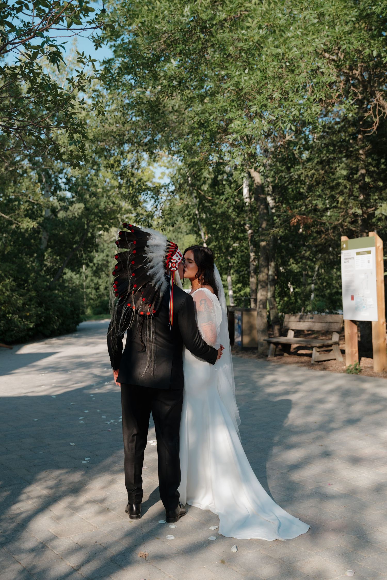A couple in wedding attire walks along a tree-lined path during an outdoor ceremony.