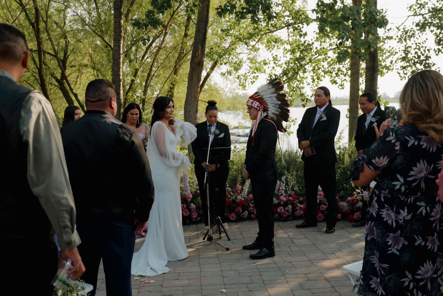 Wedding ceremony guests gather under trees and archways during an outdoor celebration.