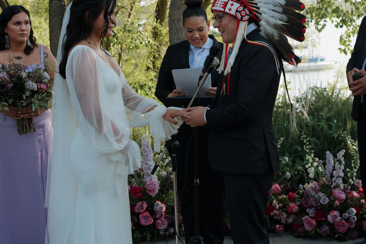 An outdoor wedding ceremony with pink floral arrangements and a Native American headdress-wearing officiant.