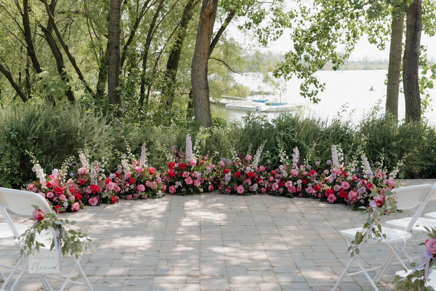 A beautiful floral arrangement with pink and red flowers decorates the ground at an outdoor wedding venue.
