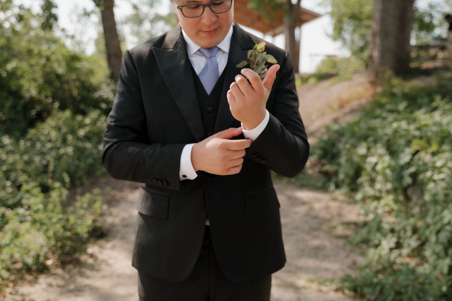 Person in formal black suit checks their phone during an outdoor event.
