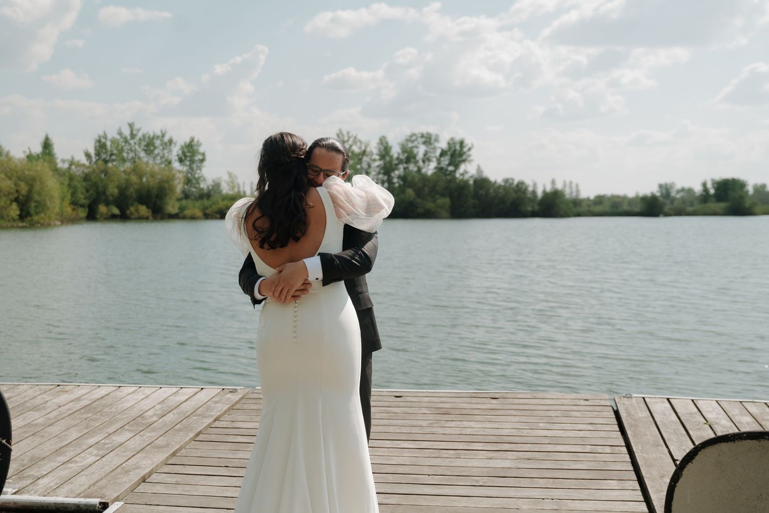 A romantic moment between newlyweds on a wooden pier overlooking a serene lake at dusk.