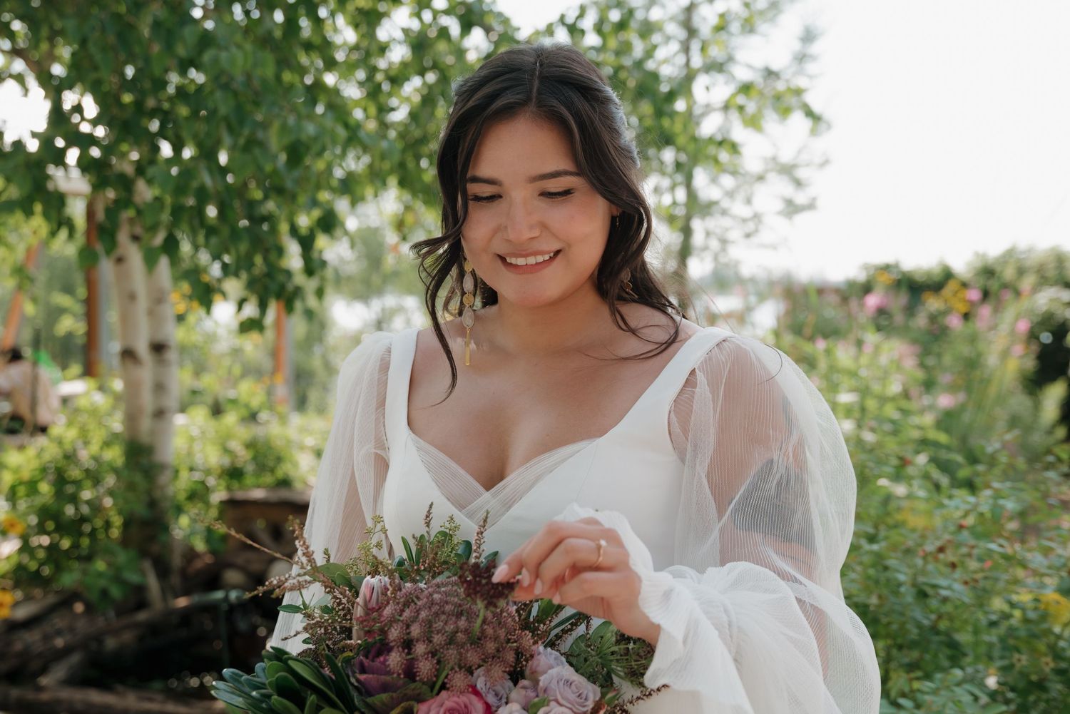 A wedding dress with sheer sleeves and a floral bouquet in an outdoor garden setting.