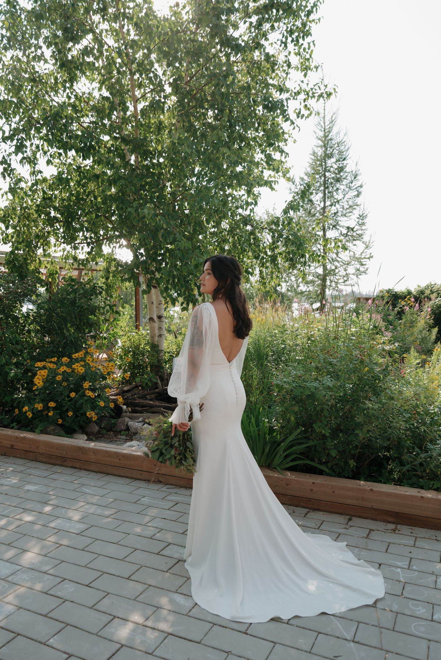 Elegant white wedding gown with flowing train photographed from behind in a garden setting.