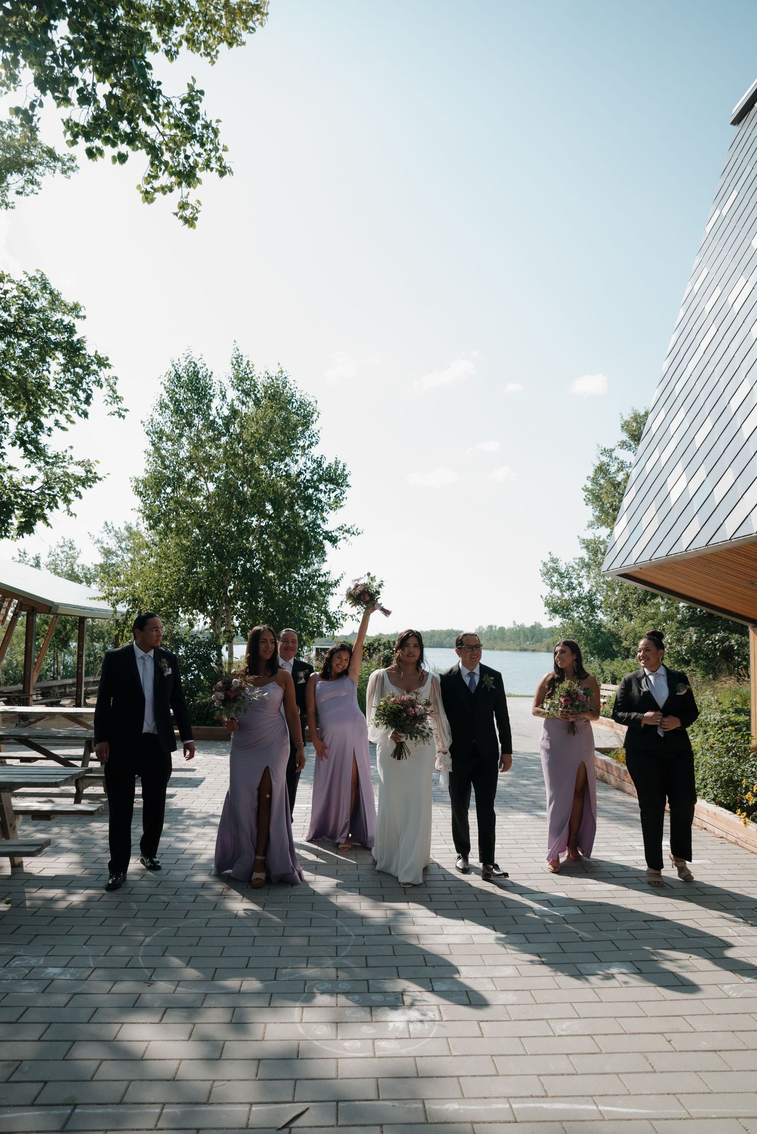 Wedding party members walk in formation along a modern architectural pathway under blue skies.